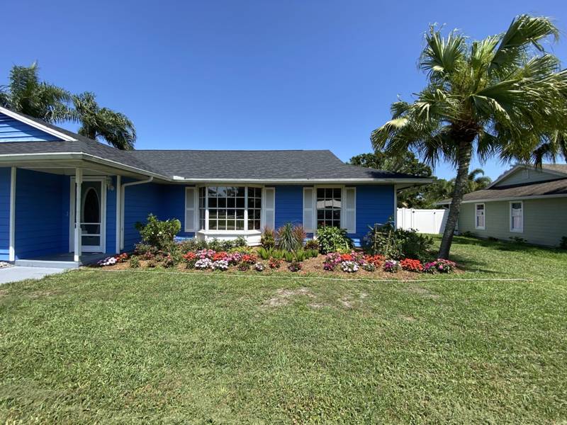 Blue house with a new lawn and a long bed of flowering annuals