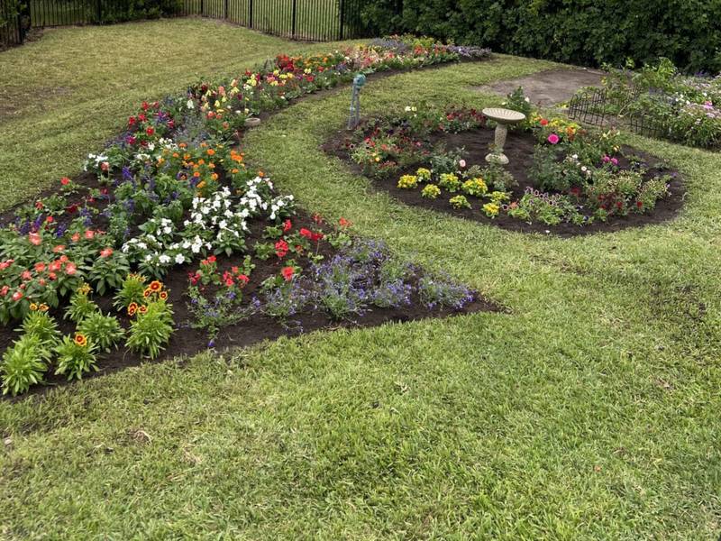 Sweeping flower beds and a round bed with a birdbath cut into a lawn beside the water