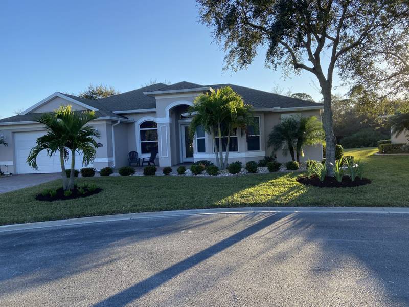 Palms and fresh mulch rings across the front lawn of a gray home