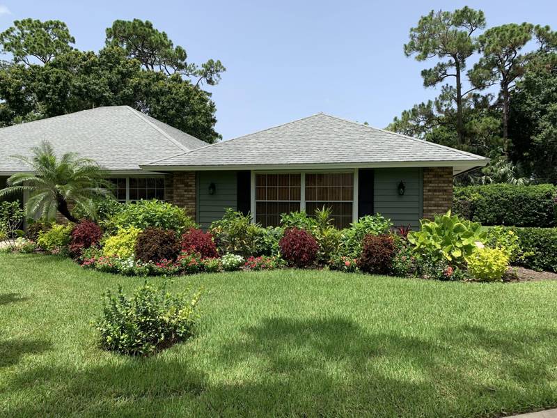 Full foundation beds of crotons and shrubs across the front of a home