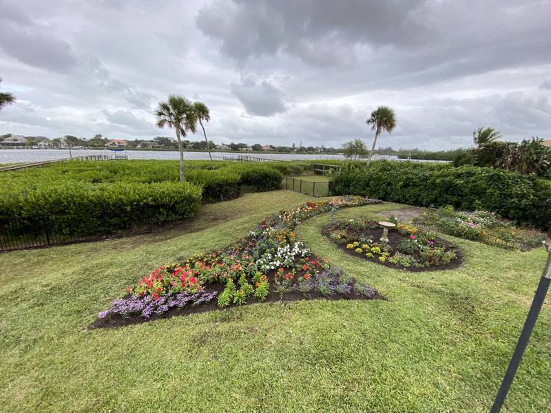 Curved flower beds on a lawn near the water under a cloudy sky