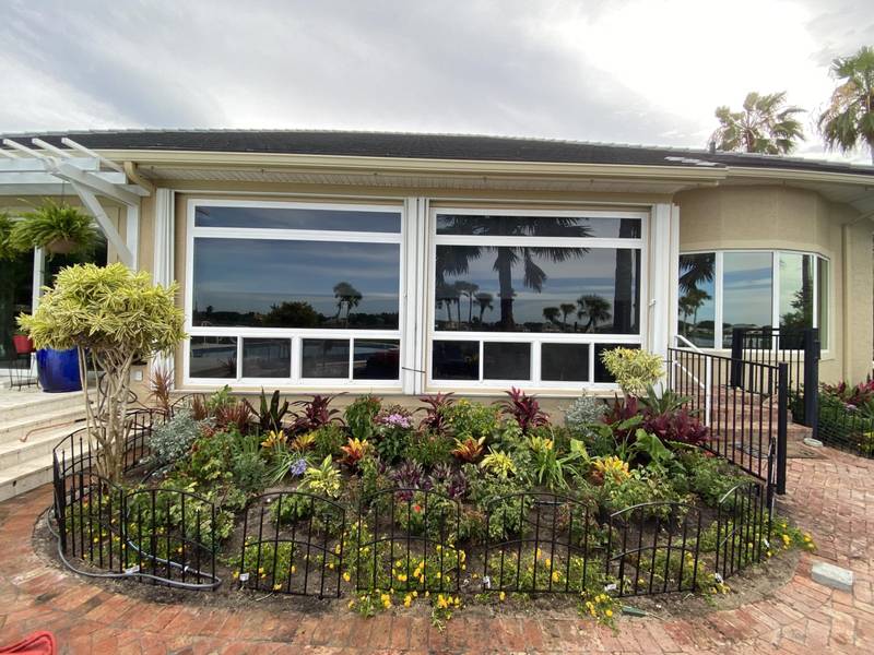 Curved flower bed with a low black garden fence in front of a home with large windows