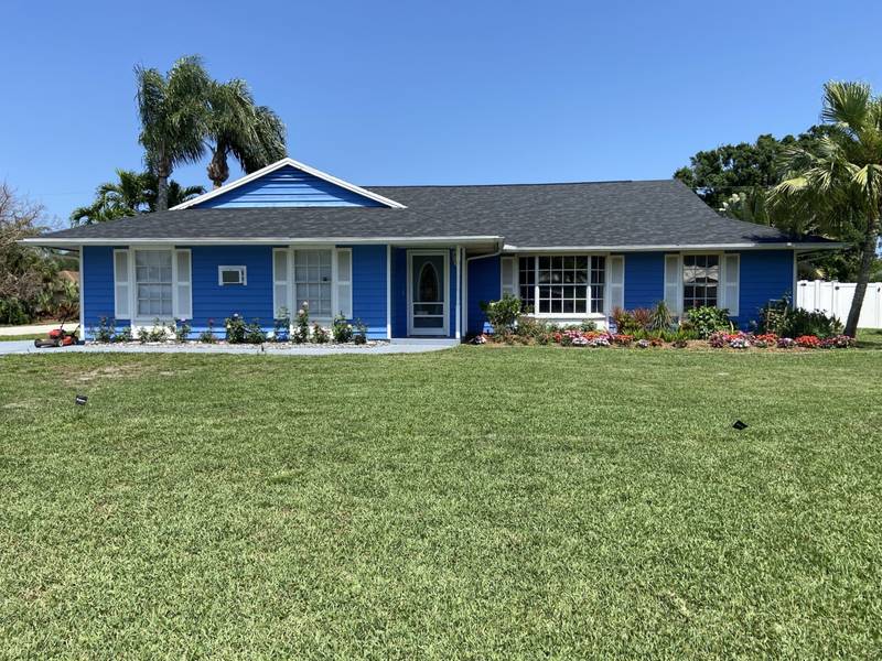 After: thick green lawn and flower beds across the front of the same blue house