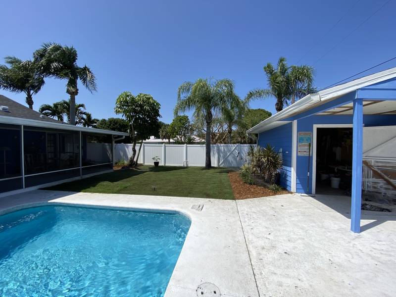 New sod laid behind a backyard pool, between a screened porch and a white fence