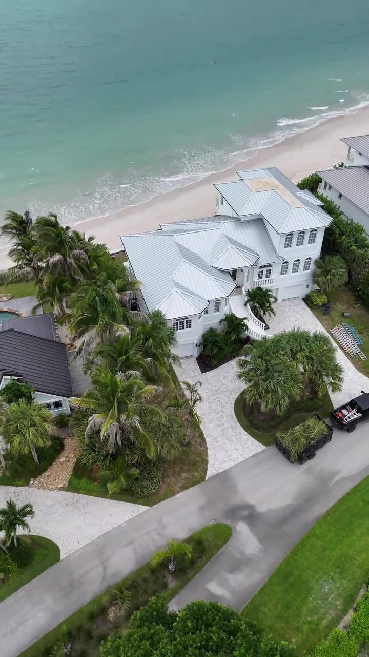 Drone shot over a beachside home and its palms, with the ocean behind